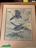 Framed artwork showing two blue jays perched on snow-covered branches over a stream, surrounded by a beige mat and light wooden frame.