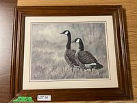 Full view of framed print showing two Canada geese on natural background with wood frame and off-white matting.