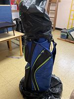 Full view of blue and black golf bag with green zipper accents closed at the top, standing upright indoors