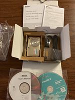 Silver Nikon Coolpix camera in original box with manuals, cables, and CDs visible