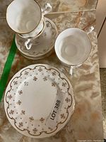 Photo showing 2 tea cups stacked on two saucers and one small plate with gold floral and trim design.
