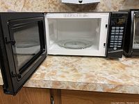 Open microwave oven showing interior with glass turntable and black door with mesh window.
