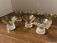 Six liqueur glasses displayed together showing clear faceted bases and decorative amber and gold bowls.