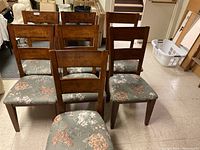 Seven wooden dining chairs with floral upholstered seats seen together in room.