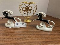 Two black and white porcelain horse figurines with a gold-toned metal heart-shaped ornament with butterfly, displayed on a neutral surface against a white background.