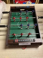 Foosball game showing full tabletop with red and blue player figures on rods, wooden frame, and score counters