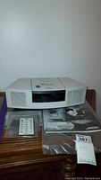 Off-white Bose Wave Radio/CD player placed on a wooden surface with accompanying remote control and manuals.