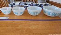 Four Pyrex mixing bowls arranged in size order on a wooden table with other dishes in background.