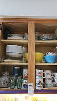 Cabinet with mid century glassware, Pyrex and Corning Ware bowls, coffee mugs, and plates.