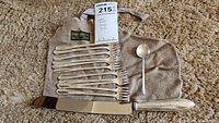 Photo shows set of 12 cocktail forks, one souvenir bamboo design spoon, Raimond stainless steele carver knife and Gimbel Brother storage bag on carpet.