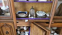 Wood cabinet shelf with various china and glass items including plates, bowl, salt and pepper shakers, biscuit jar
