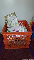Orange plastic crate filled with greeting cards and stationery including envelopes.