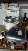 Wide view showing Rival crock pot, Sunbeam electric pan, utensils, and Cuisinart food processor box with cookware and chopper