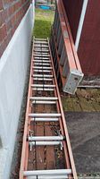 Photo showing the 28 ft orange extension ladder with aluminum rungs laid out outside on a brick and concrete surface leaning against a wall.