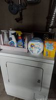 Lot of laundry and cleaning supplies placed on dryer.