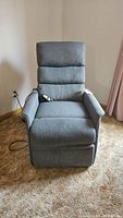 Front view of the grey fabric lift recliner chair showing remote control on armrest, chair in reclined position.