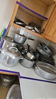 Overview of the lot showing stacked pots and pans and some lids in a kitchen cabinet and countertop