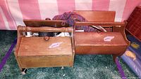 Two wooden vintage sewing caddies holding various sewing and crochet supplies placed on a carpet with pink and white striped fabric in background.