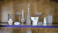 Wide front view showing cut glass Waterford decanter with stopper, hobnail fan edge vase, two tall cut glass compote bowls and small decorative pieces arranged on shelf.