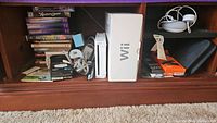 Photo of Nintendo Wii console with its box, various DVDs, VHS tapes, cords, and headphones.