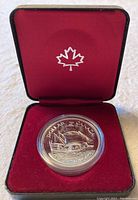 Front view of silver dollar coin in red display case with maple leaf emblem inside lid