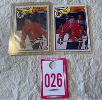 Two O-PEE-CHEE hockey cards in protective sleeves, Steve Larmer #105 and Steve Ludzik #106 with swapped photos error, accompanied by a bidding number tag.