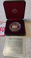Opened black and red velvet display case with silver coin inside and certificate card showing details of the coin.