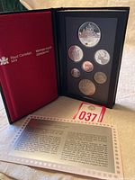 Opened proof coin set case showing seven Canadian coins ranging from 1 cent to 2 dollars with red interior and Royal Canadian Mint branding, including informational card.