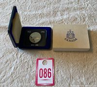 Commemorative coin in blue display case next to outer cardboard box and auction tag