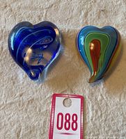 Two heart-shaped glass paperweights on a textured surface with a numbered tag 088