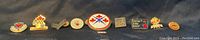 Wide shot of 10 small military themed pins including colorful enamel designs and military insignia
