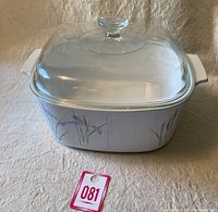 Photo showing full front view of the white square Corning Ware casserole dish decorated with purple Shadow Iris flowers and green stalks, topped with a clear Pyrex glass lid with knob handle.