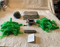 Top down photo showing entire lot: two fishing reels, metal tackle box, Swiss Army style pocket knife, and clusters of bright green fishing lures.