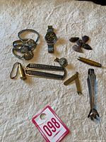 Full lot laid out on a stone surface showing all items: rings, watch, arrowheads, bullet casing, multi-tool, pin, tie clip, and Reed & Prince box.