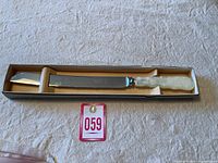 Full view of the vintage wedding cake cutter in its original box, showing the entire length of the stainless steel blade and the faux mother-of-pearl handle.