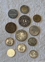 Top view of 11 assorted world coins arranged on a white textured fabric background showcasing different designs and sizes.