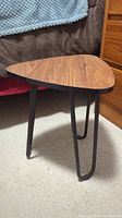 Side angle view of the mid-century modern style small end table showing wood grain top and black hairpin legs.