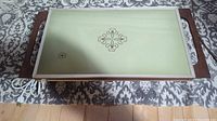 Top view of the warming tray showing pale green surface with decorative floral detail and wood handles on each side.