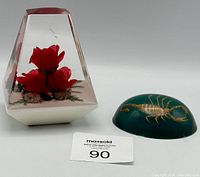 Two resin decorative pieces: a geometric resin piece with red roses and a green resin oval with a scorpion inside; lot number tag included.