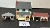 Photo of three HO scale buildings including a house, garage, and gazebo, showing front and partial side views on a flat surface.