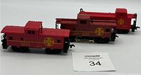 Three red HO scale Santa Fe caboose cars arranged side by side on a white surface with a MaxSold lot number card visible.