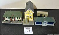 Four HO scale model train buildings including houses, bank, and outbuilding arranged on black surface