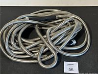 Flexible metal hose coiled on a black surface with threaded ends visible.