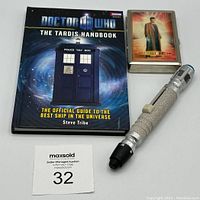 Lot display of The TARDIS Handbook, metal case with character image, and sonic screwdriver prop
