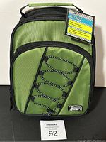 Front view of green Gear Tech insulated lunch bag with attached tag and bungee cord on front pocket.