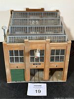 Front view of HO scale train building car shop with detailed window sections, green garage door, and central light fixture above a labeled sign.