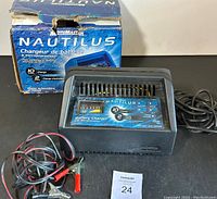 Overall front view of the MotoMaster Nautilus black battery charger with cables and original box in background.