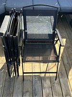 Four black outdoor folding chairs, one opened showing mesh seating and armrests, others folded and lined up.