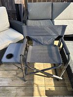 Front view of a black outdoor folding chair with mesh seat and back, showing the pop-out side table with cup holder attached to the armrest.