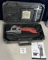 Full view of open carrying case showing RotoRazor Platinum RZ200B compact circular saw, power cord, extra blade in plastic case, hex key, metal square tool, and user manual.